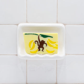 Monkey Business Vegetable Glycerin Bar Soap in a white soap dish on a tiled bathroom wall.