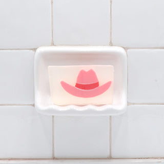 Pink Cowboy Hat Vegetable Glycerin Bar Soap in a white soap dish on a tiled bathroom wall.