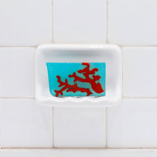 Red Coral Vegetable Glycerin Bar Soap in a white soap dish on a tiled bathroom wall.