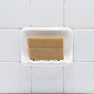 Rhassoul Clay Vegetable Glycerin Bar Soap in a white soap dish on a tiled bathroom wall.