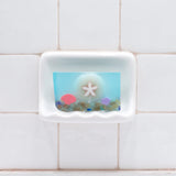 Sand Dollar Vegetable Glycerin Bar Soap in a white soap dish on a tiled bathroom wall.