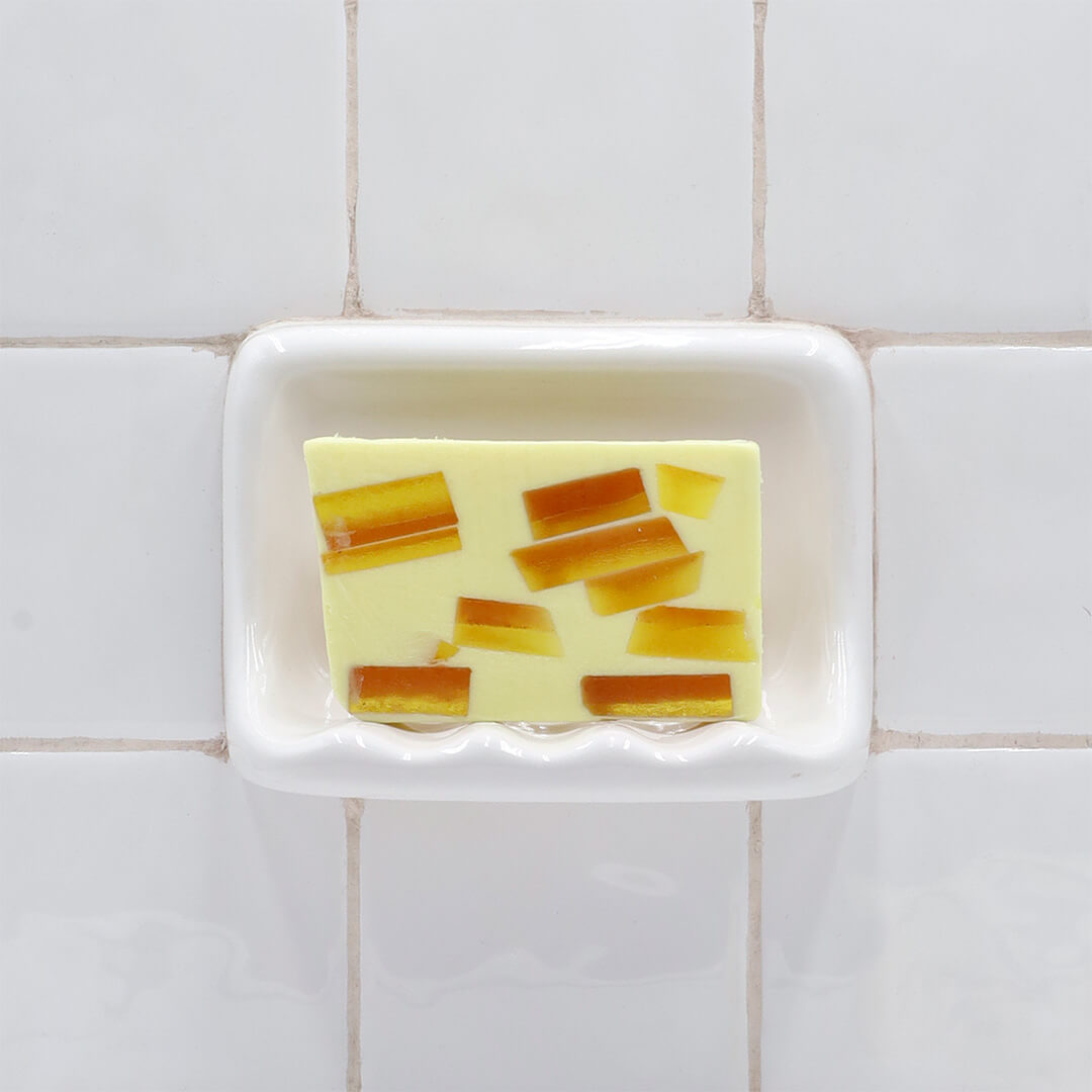 Tahitian Vanilla Vegetable Glycerin Bar Soap in a white soap dish on a tiled bathroom wall.
