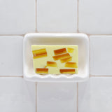 Tahitian Vanilla Vegetable Glycerin Bar Soap in a white soap dish on a tiled bathroom wall.