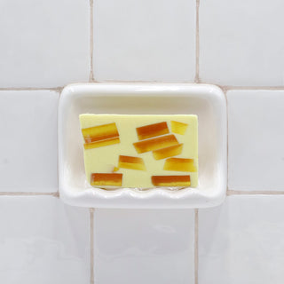 Tahitian Vanilla Vegetable Glycerin Bar Soap in a white soap dish on a tiled bathroom wall.