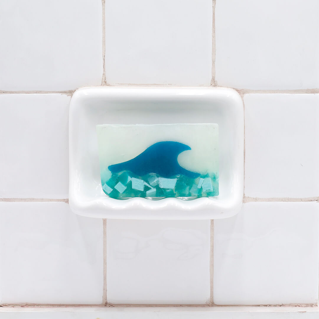 Tranquility Vegetable Glycerin Bar Soap in a white soap dish on a tiled bathroom wall.