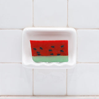 Watermelon Vegetable Glycerin Bar Soap in a white soap dish on a tiled bathroom wall.