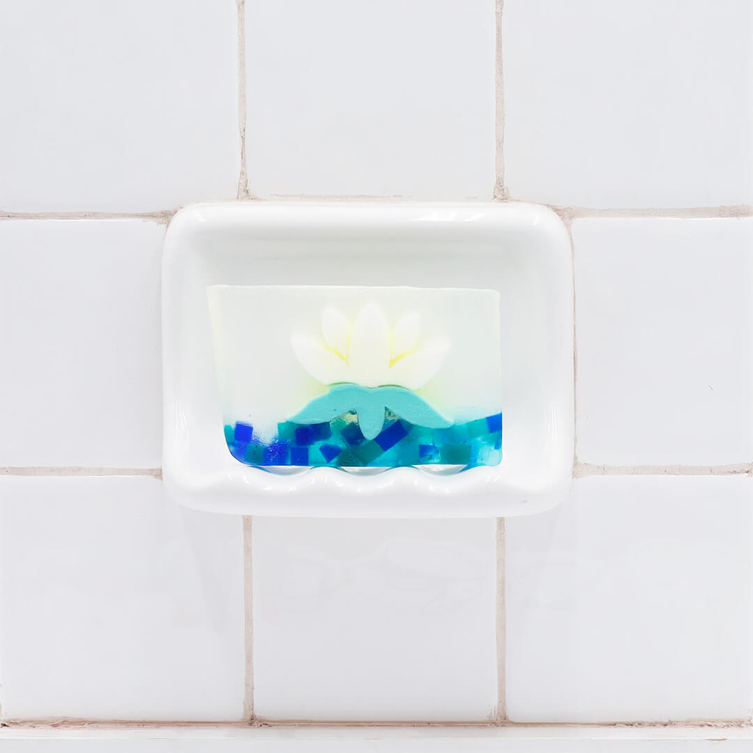White Lotus Vegetable Glycerin Bar Soap in a white soap dish on a tiled bathroom wall.